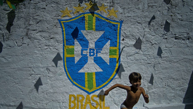 A boy runs past graffitti showing the Brazil logo