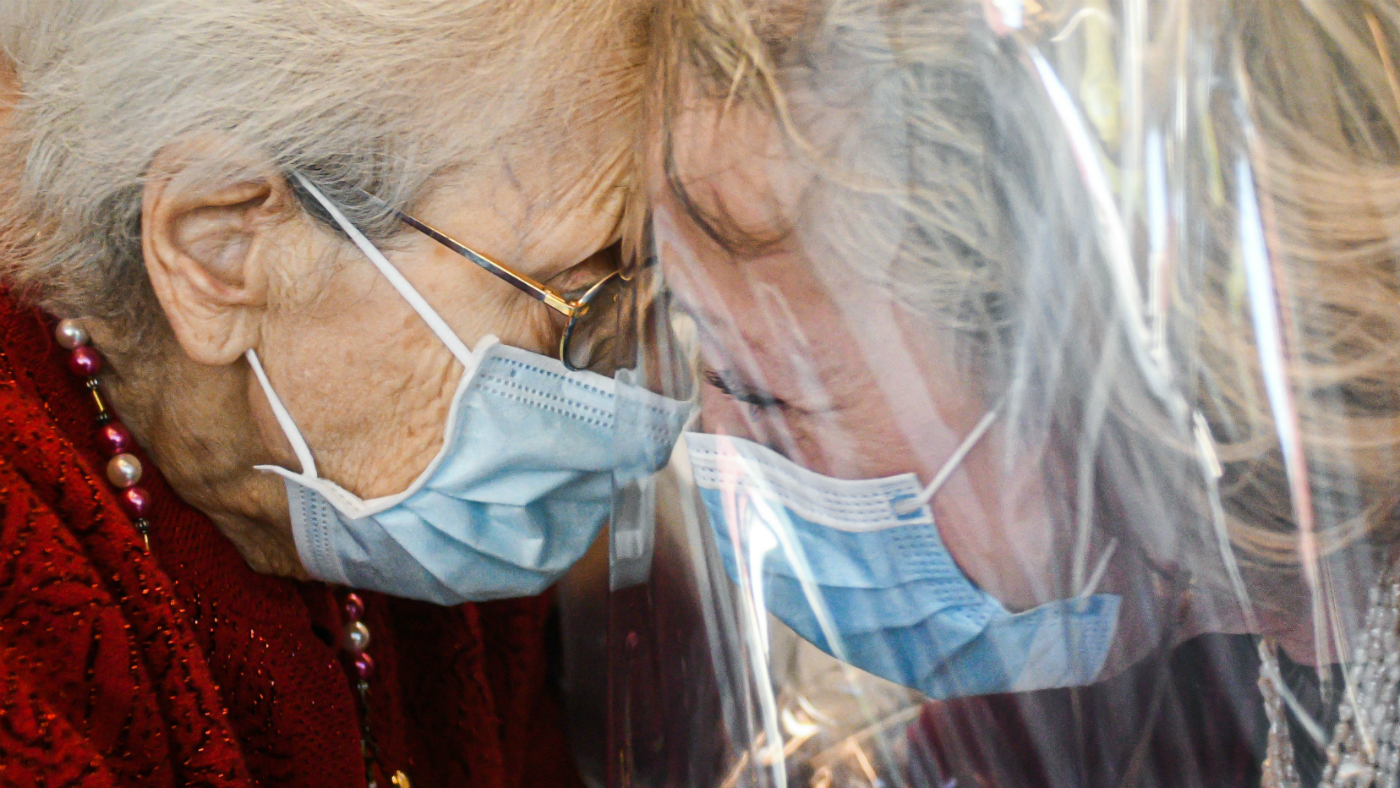 Two elderly people wearing face masks are reunited. 