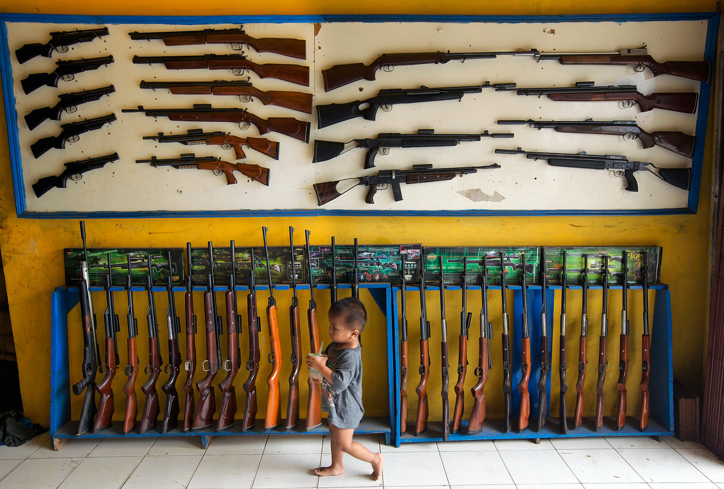 CIPACING, INDONESIA - MARCH 4: The son of the owner of an air rifle shop walks past air rifles on display at the shop nearby dozens of small air rifle workshops on March 4, 2014 in Cipacing, 