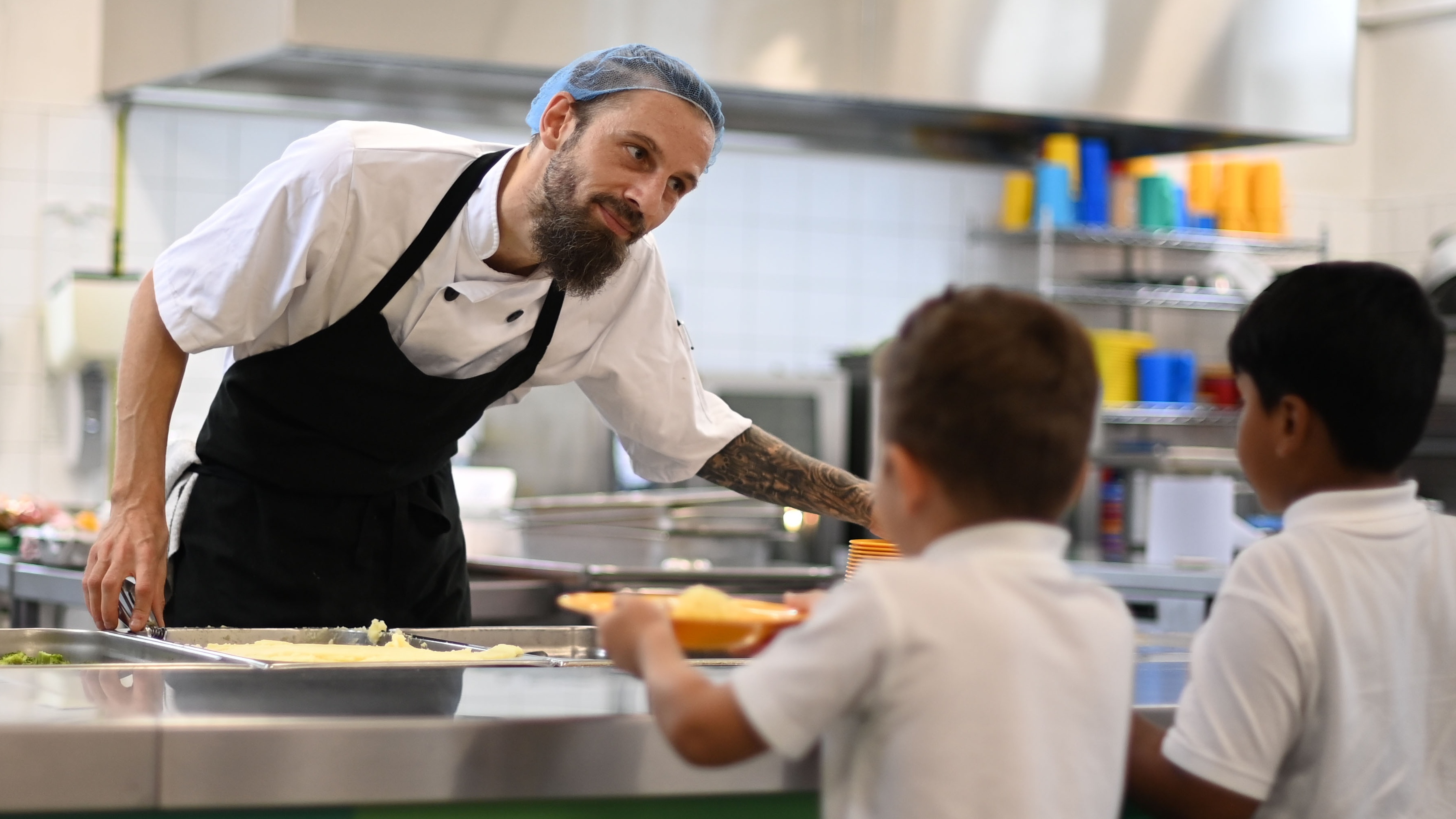 A school chef serves cooked hot dinner to students on their lunch break 