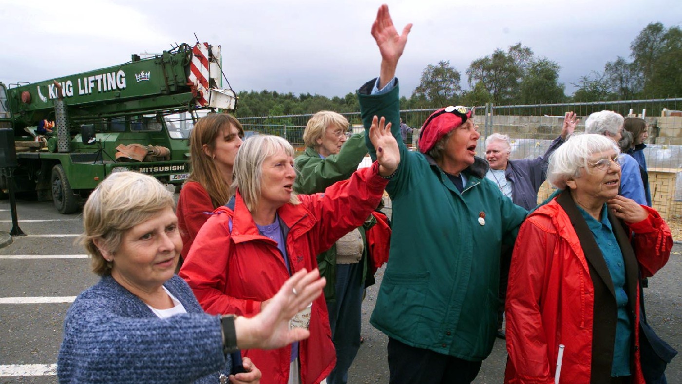 Peace campaigners wave as their caravan is taken away from outside the gates of Greenham Common on 5 September 2000