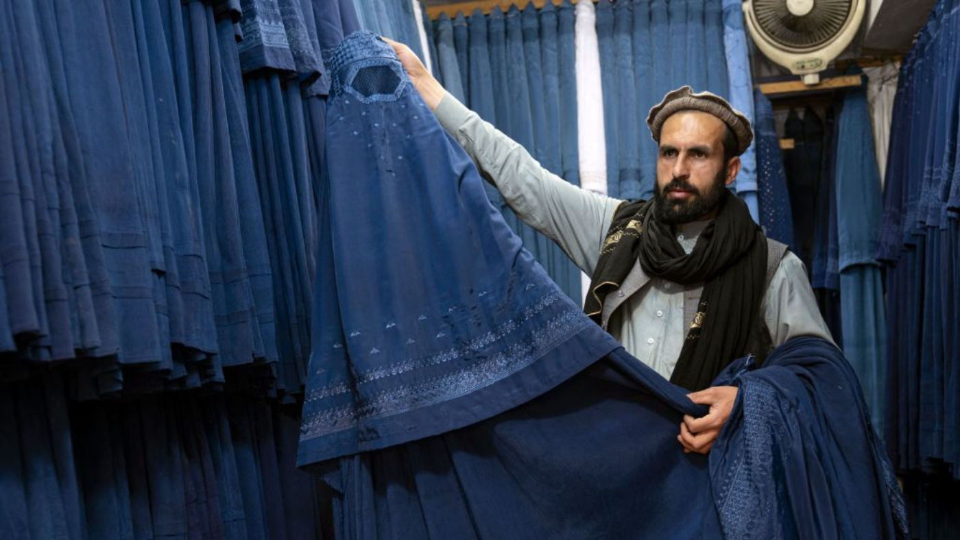 A burqa vendor holds out his goods at a market in Kabul