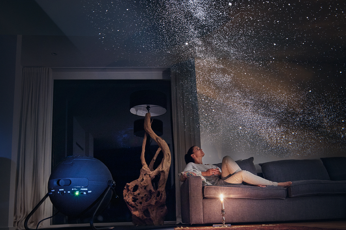 Woman sat on sofa looking at projection of stars on ceiling