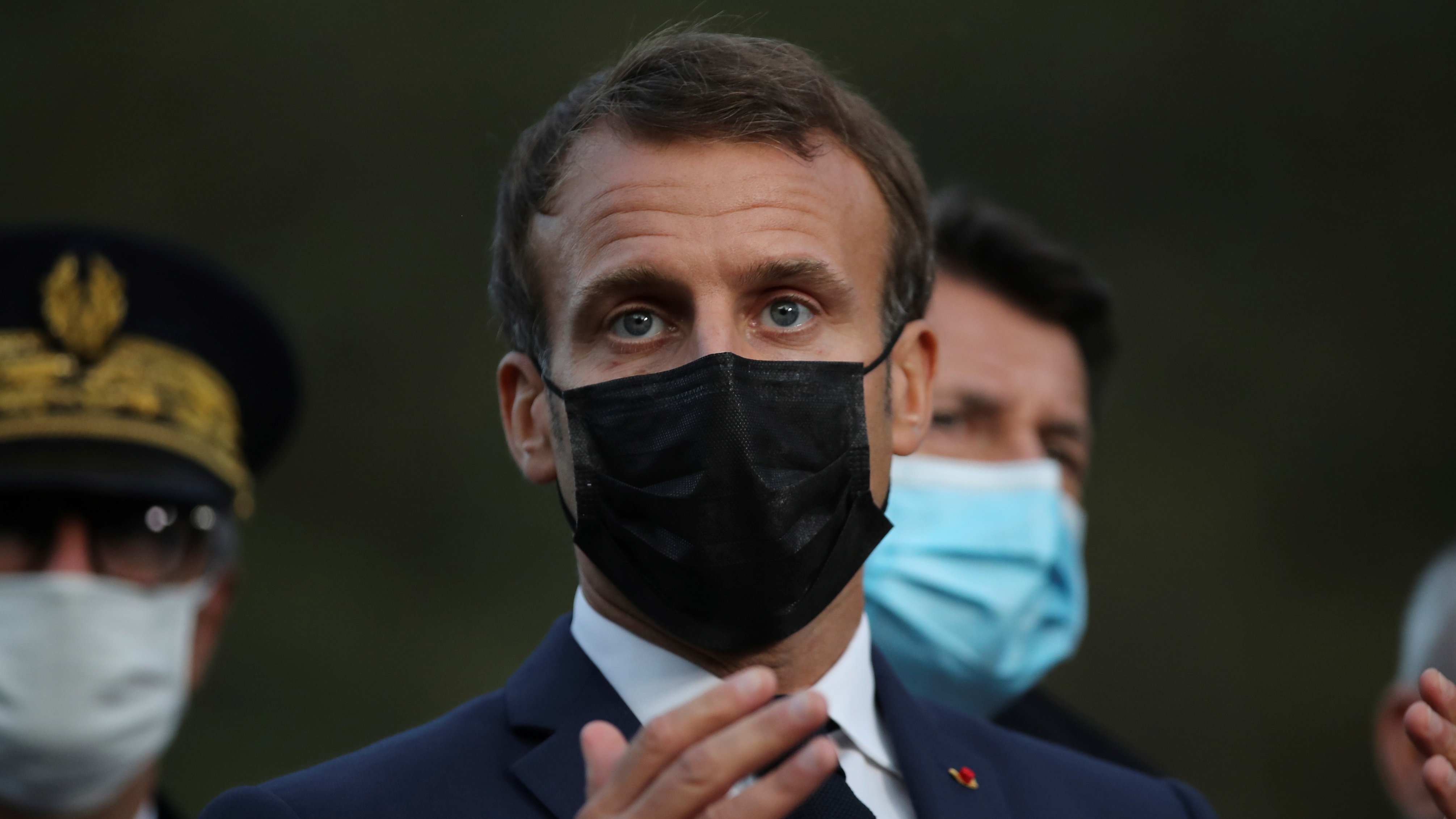 Emmanuel Macron addresses journalists wearing a black face mask/
