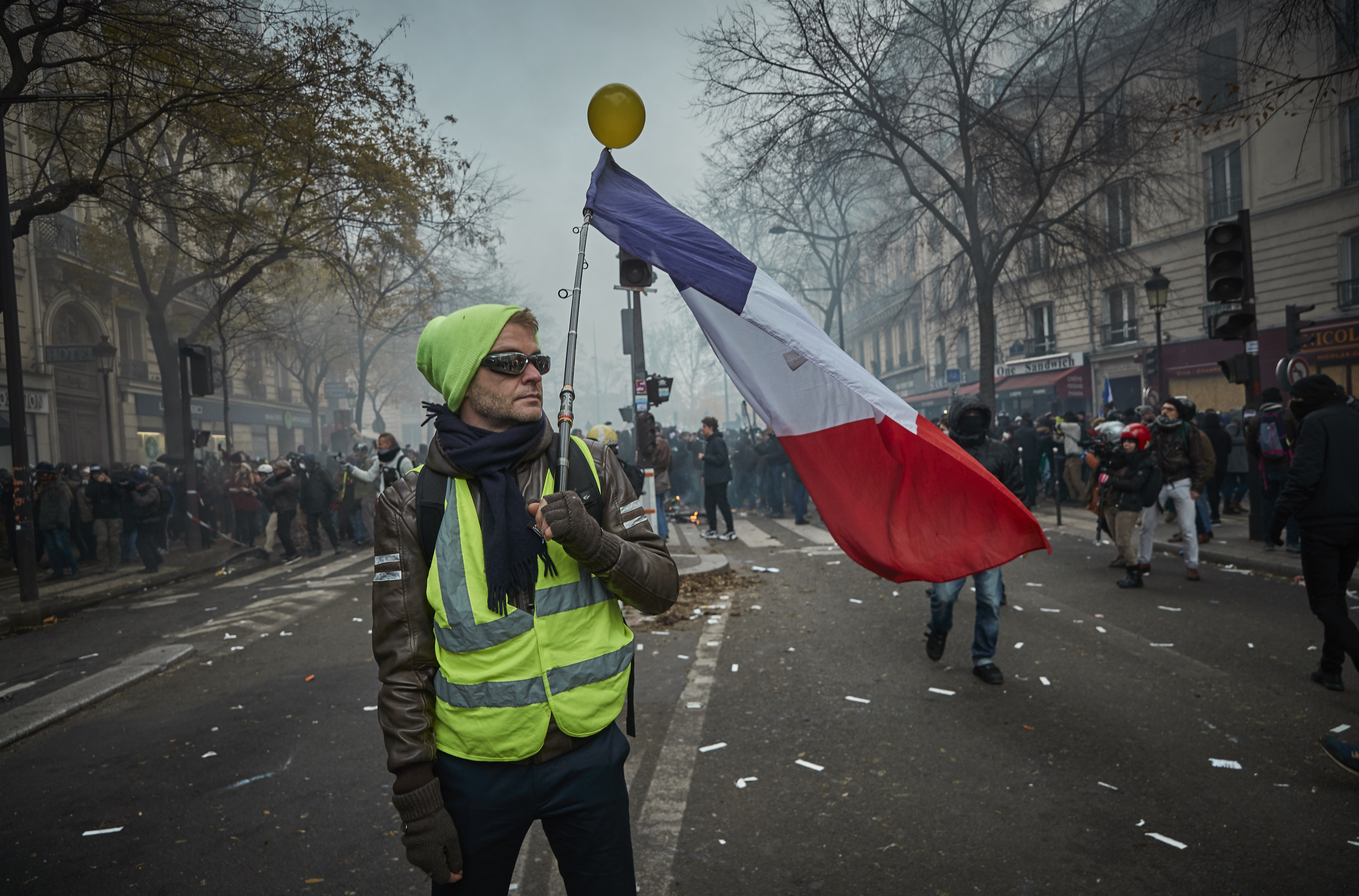 PARIS, FRANCE - DECEMBER 05: A Gilet Jaune, or Yellow Vest&#039; holds a French Tricolor amidst tear gas as protestors and French Riot Police clash during a rally near Place de Republique in suppo