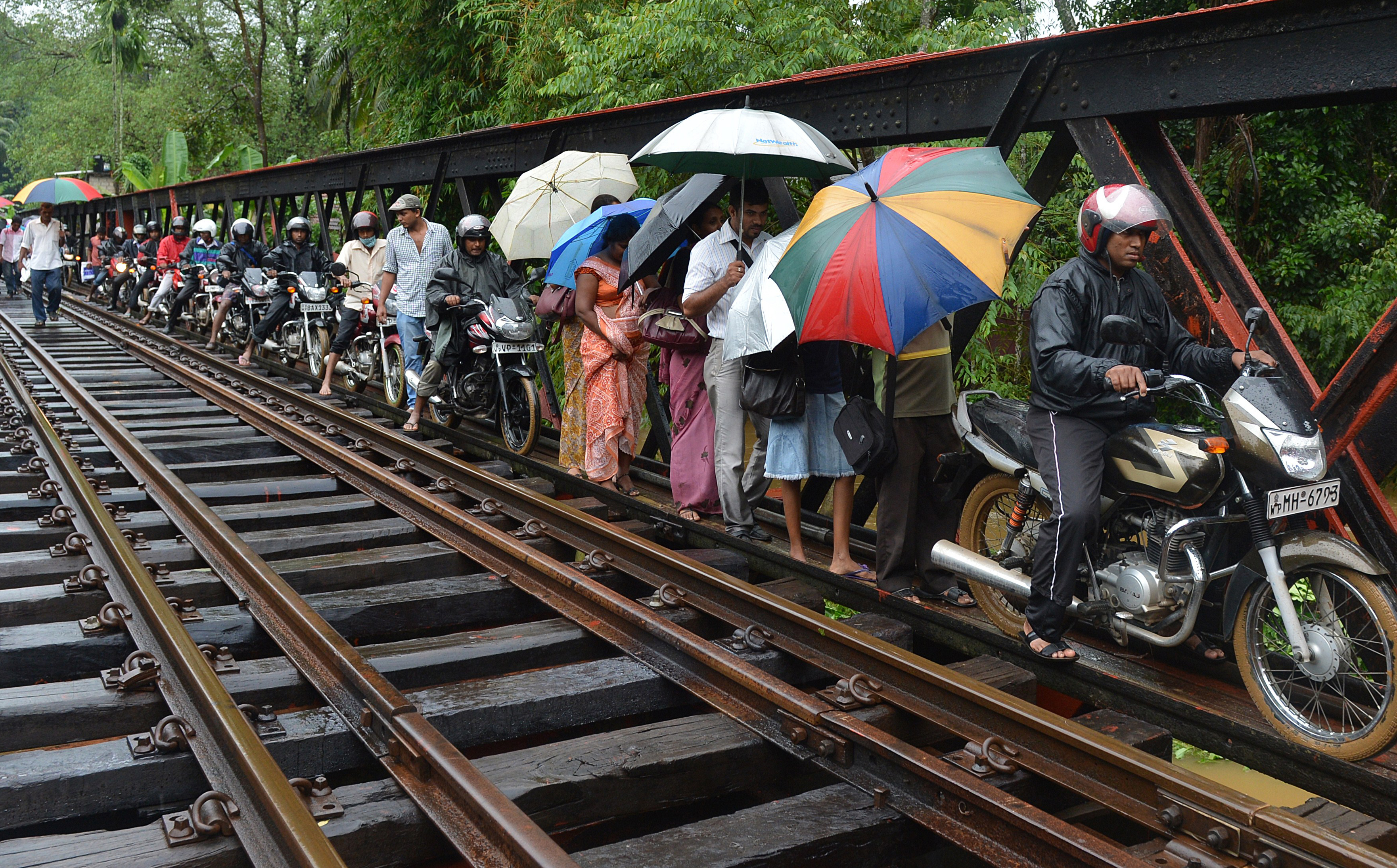 Sri Lankan flood victims cross a narrow access path along a railroad bridge in Puwakpitiya on June 3, 2014 after heavy monsoon rans caused havoc in the western, southern and central regions o
