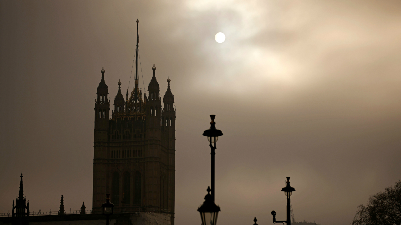 The sun shines through clouds over the Palace of Westminster.