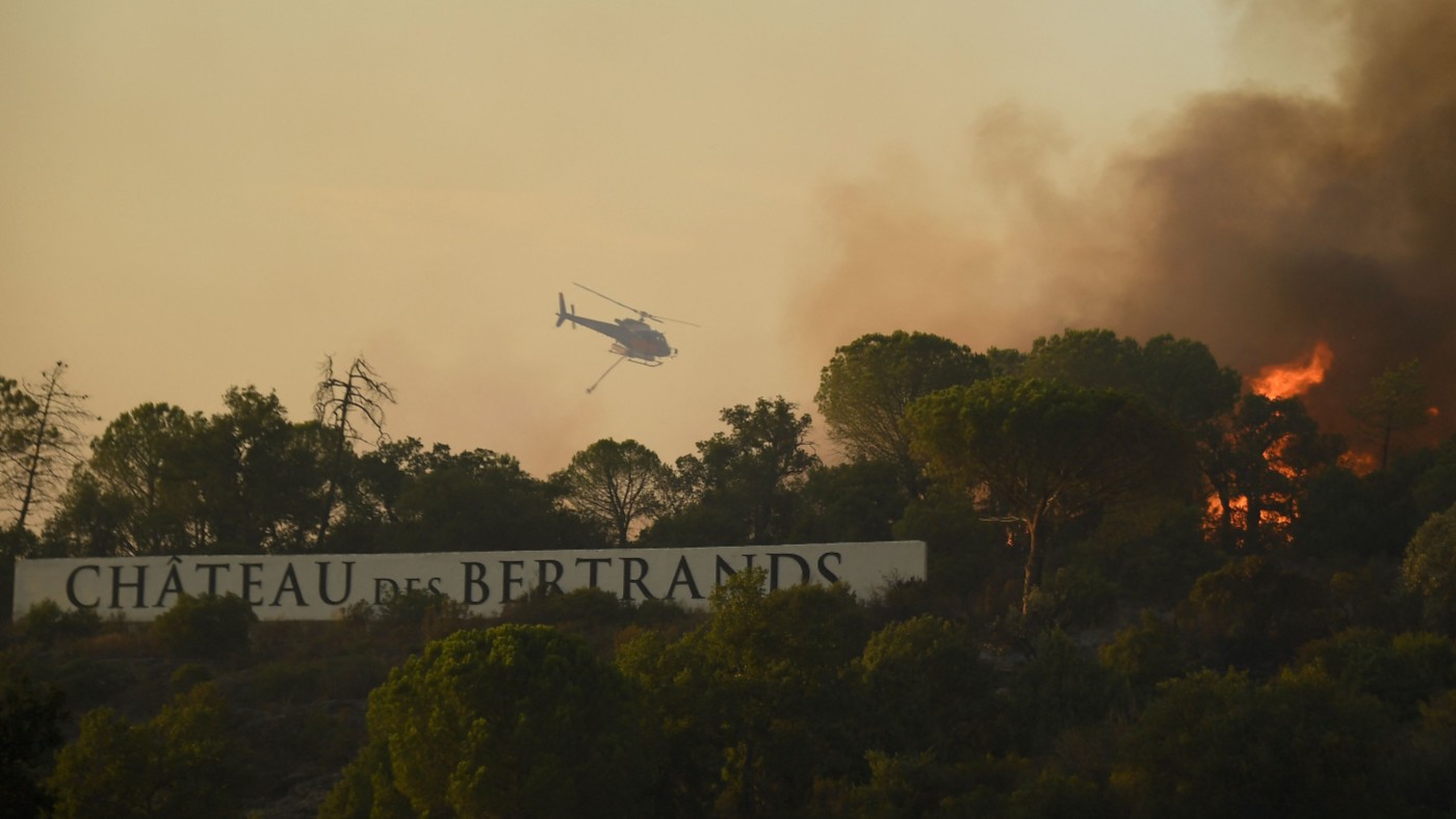 A firefighting helicopter flies above a wildfire near the Château des Bertrands winery in the Var region of Provence, France  