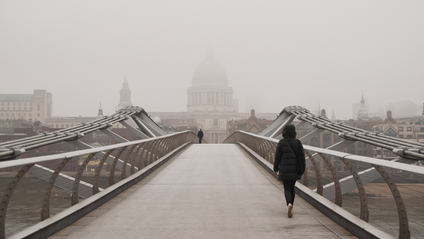 Person walks over Millennium Bridge in London during winter fog