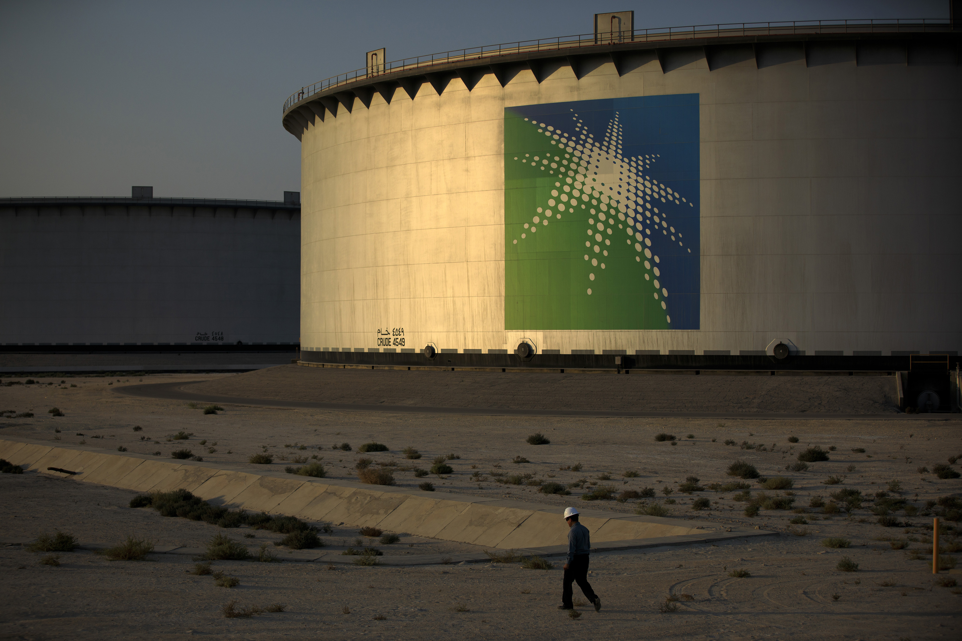 An employee walks past crude oil storage tanks at the Juaymah Tank Farm in Saudi Aramco&#039;s Ras Tanura oil refinery and oil terminal in Ras Tanura, Saudi Arabia, on Monday, Oct. 1, 2018. Saudi 
