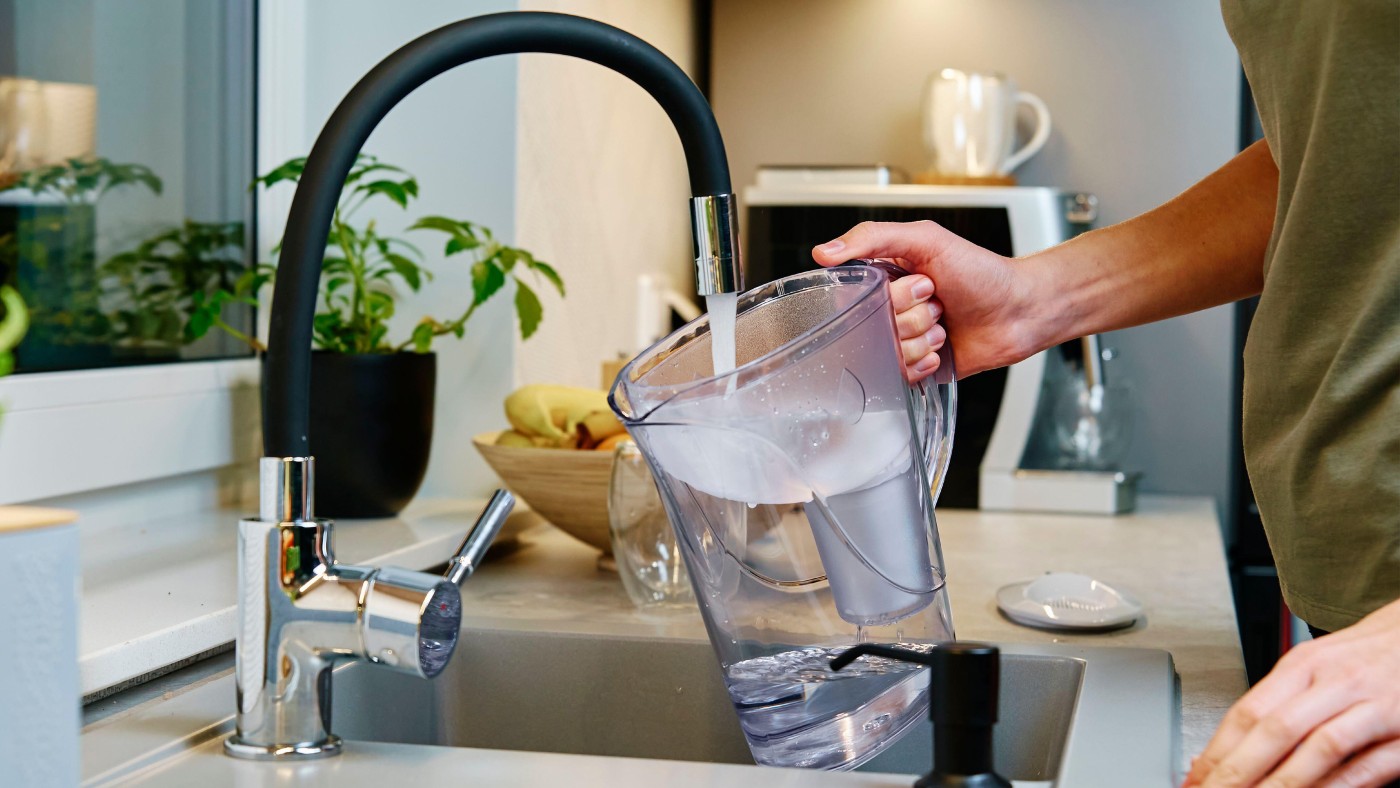 Woman pouring water from a tap into a water filter jug  