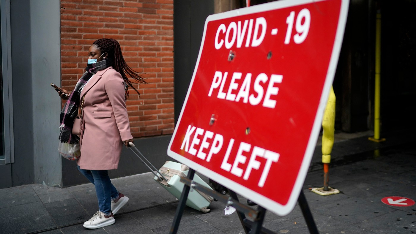 A masked woman passes a Covid lockdown sign