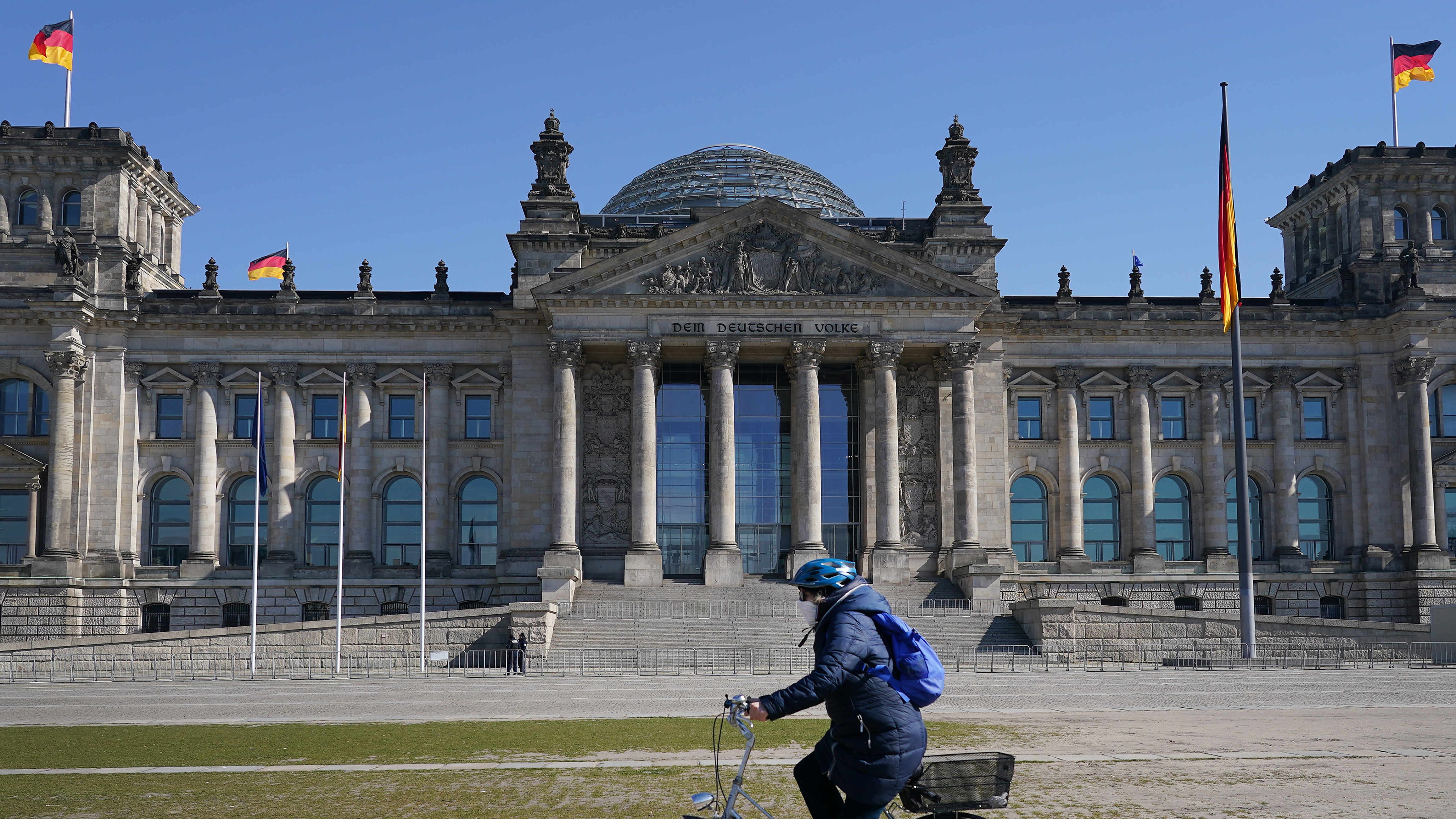 A woman cycles past the Reichstag in Berlin wearing a face mask in March 2020