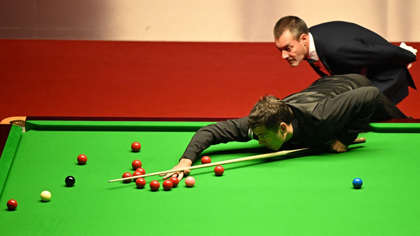 Ronnie O’Sullivan plays a shot left-handed as referee Olivier Marteel watches on