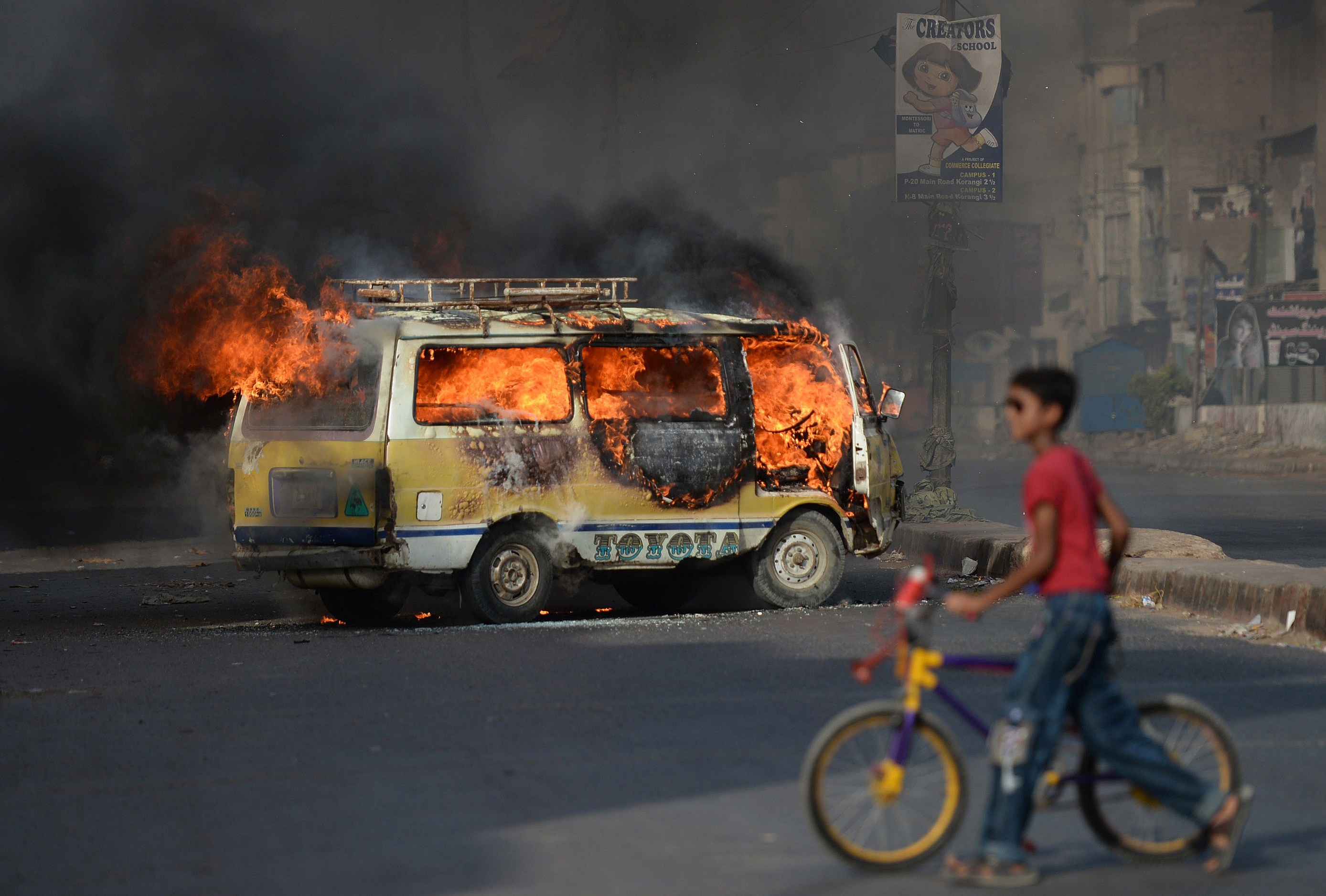 A Pakistani youth wheels his bicycle past a burning vehicle on a street in Karachi on June 3, 2014 following the arrest of Altaf Hussain, head of Pakistan&#039;s Muttahida Qaumi Movement (MQM) par
