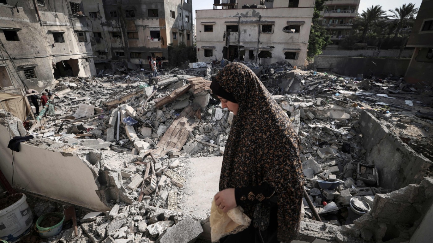 A Palestinian woman walks through rubble in front of her home in Gaza