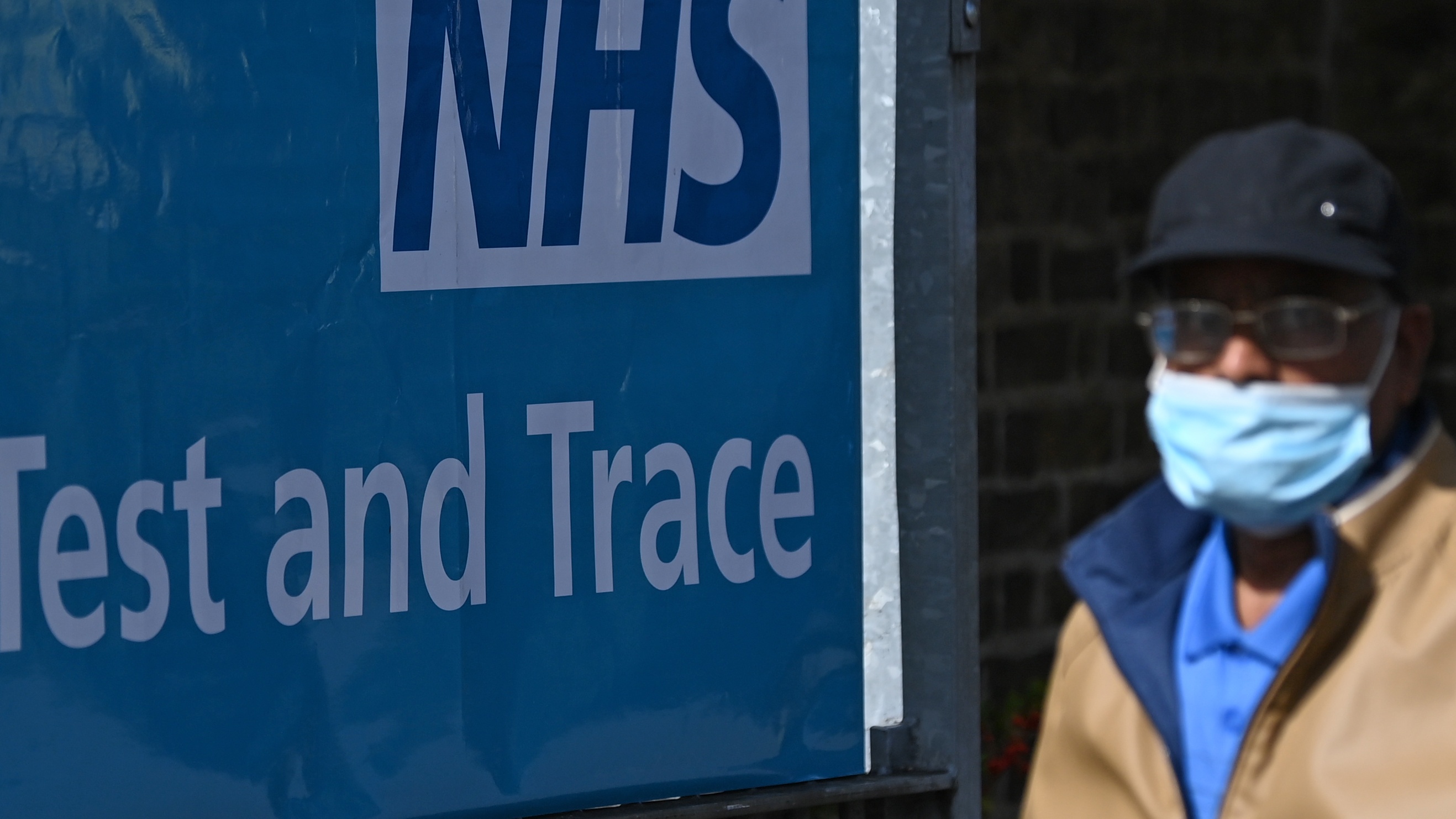 A man wearing a face mask passes a sign for the NHS test-and-trace service.