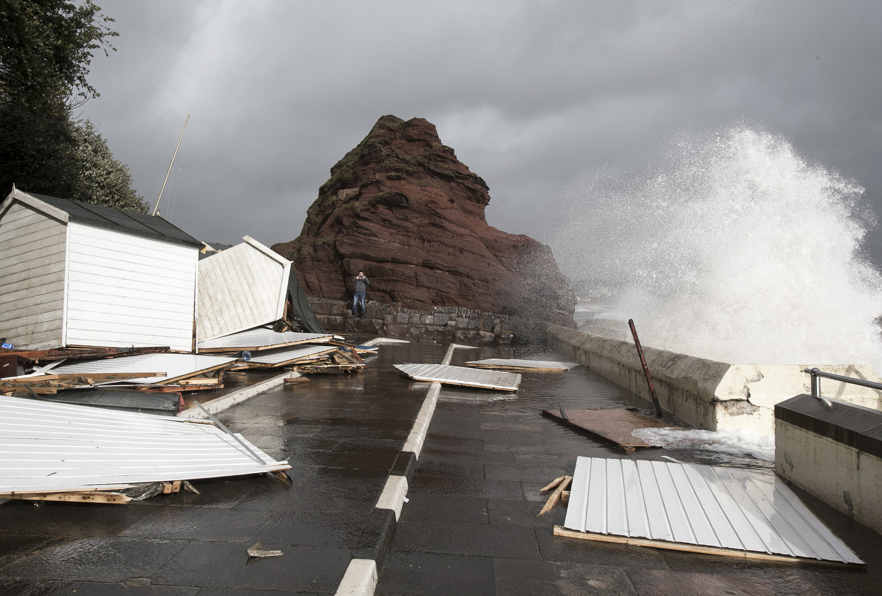 DAWLISH, UNITED KINGDOM - FEBRUARY 05:A man takes a photograph of some of the beach huts that have been damaged by the storm waves at Dawlish on February 5, 2014 in Devon, England. With high 