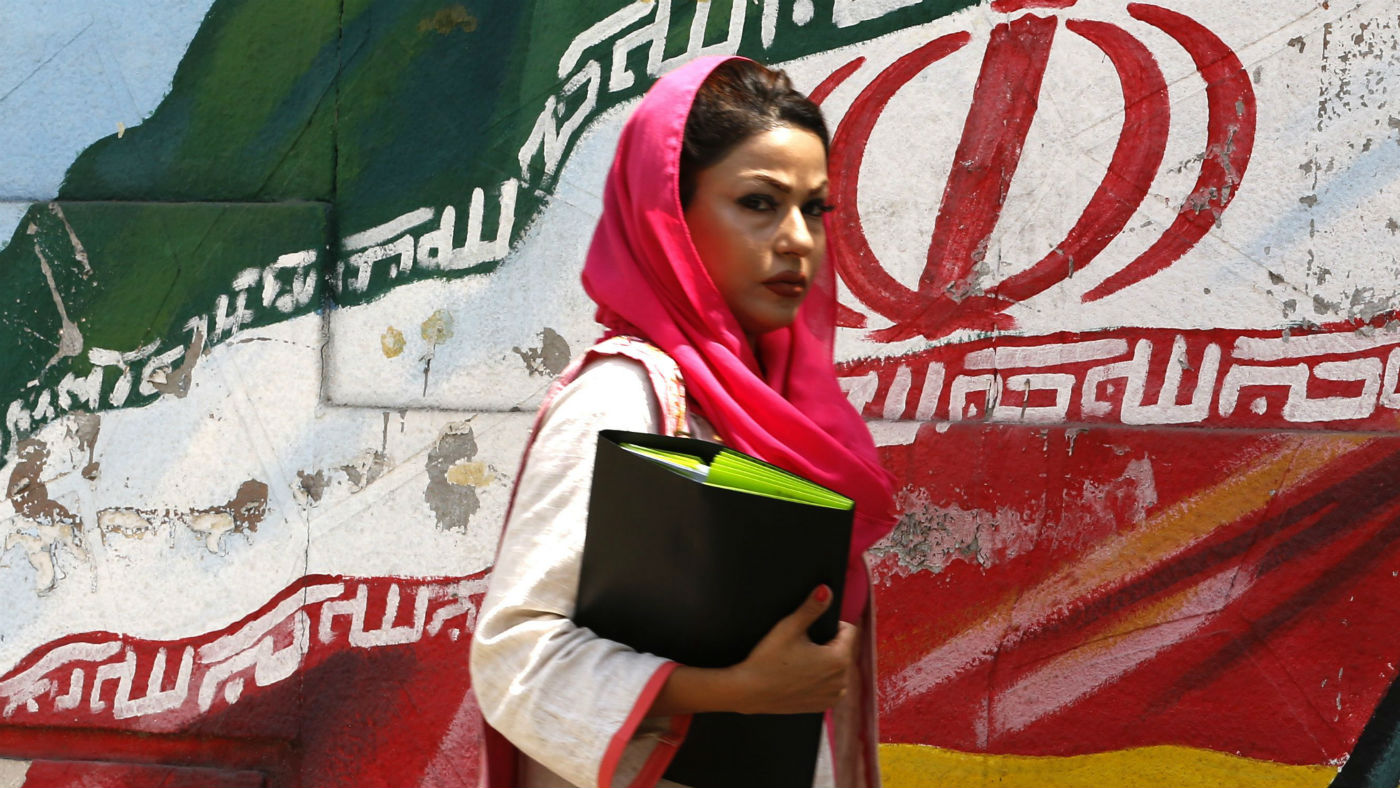 A woman walks in front of a mural painting depicting the Iranian flag, in the capital Tehran
