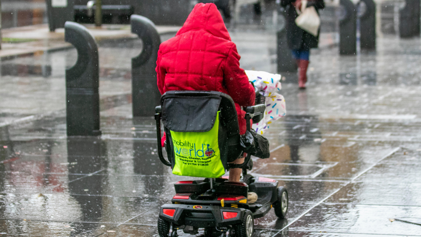 A wheelchair user on a rainy pavement