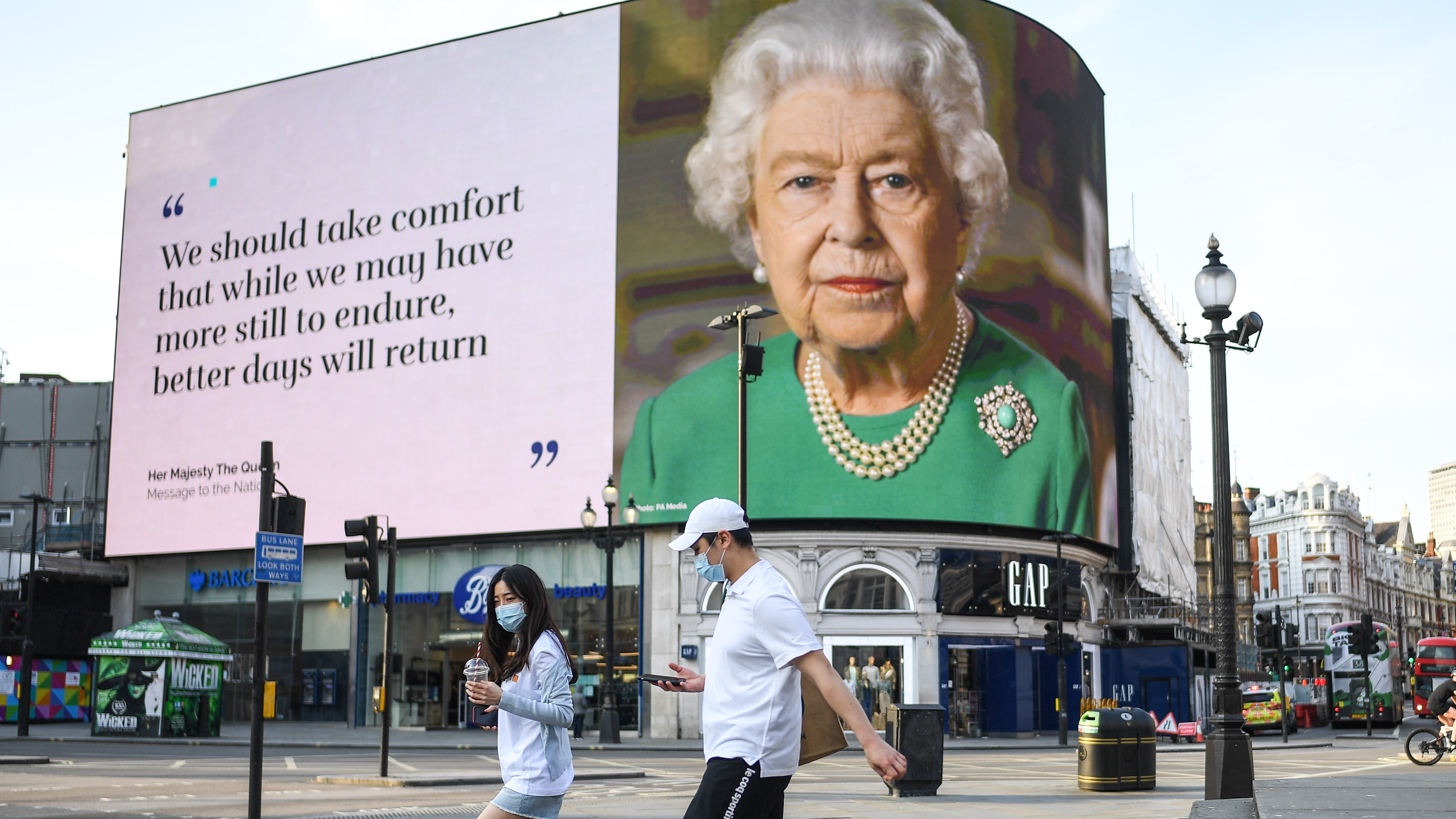 A couple wearing masks walk past an image of Queen Elizabeth II.
