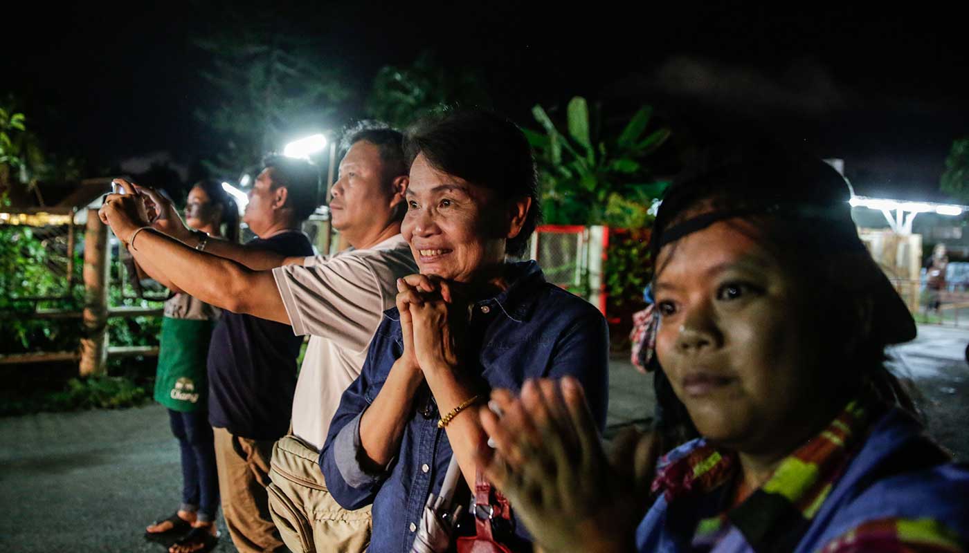 Onlookers smile as they watch an ambulance carrying boys rescued from the cave