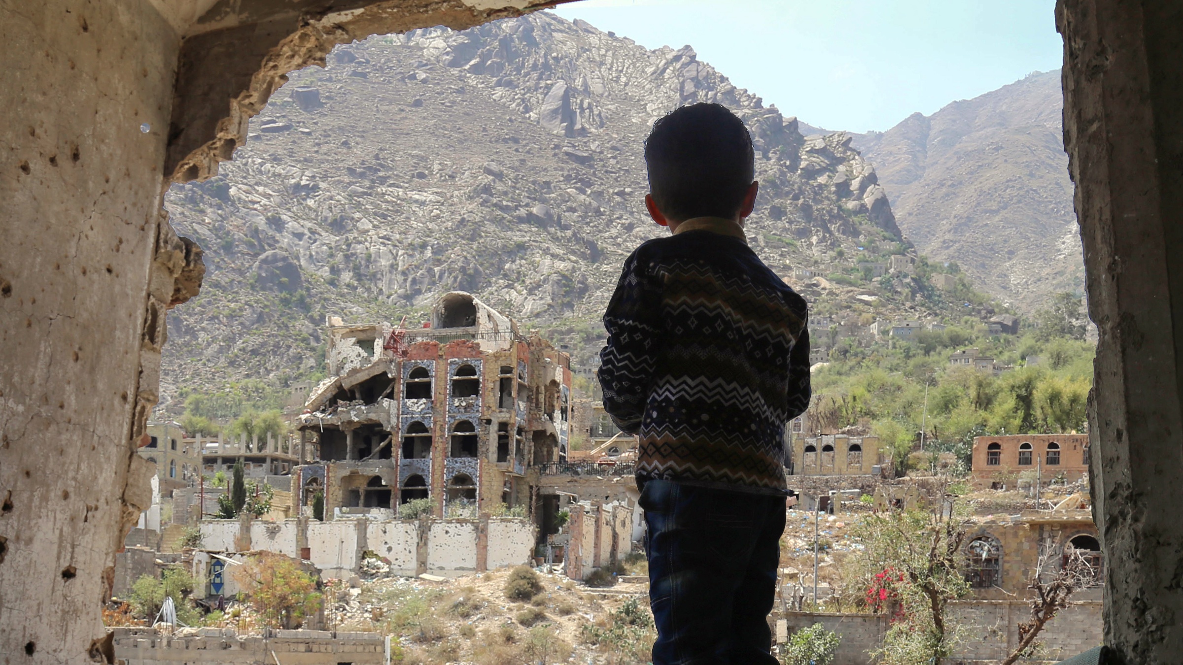 A child looking out at buildings destroyed by an air strike in Taiz, Yemen