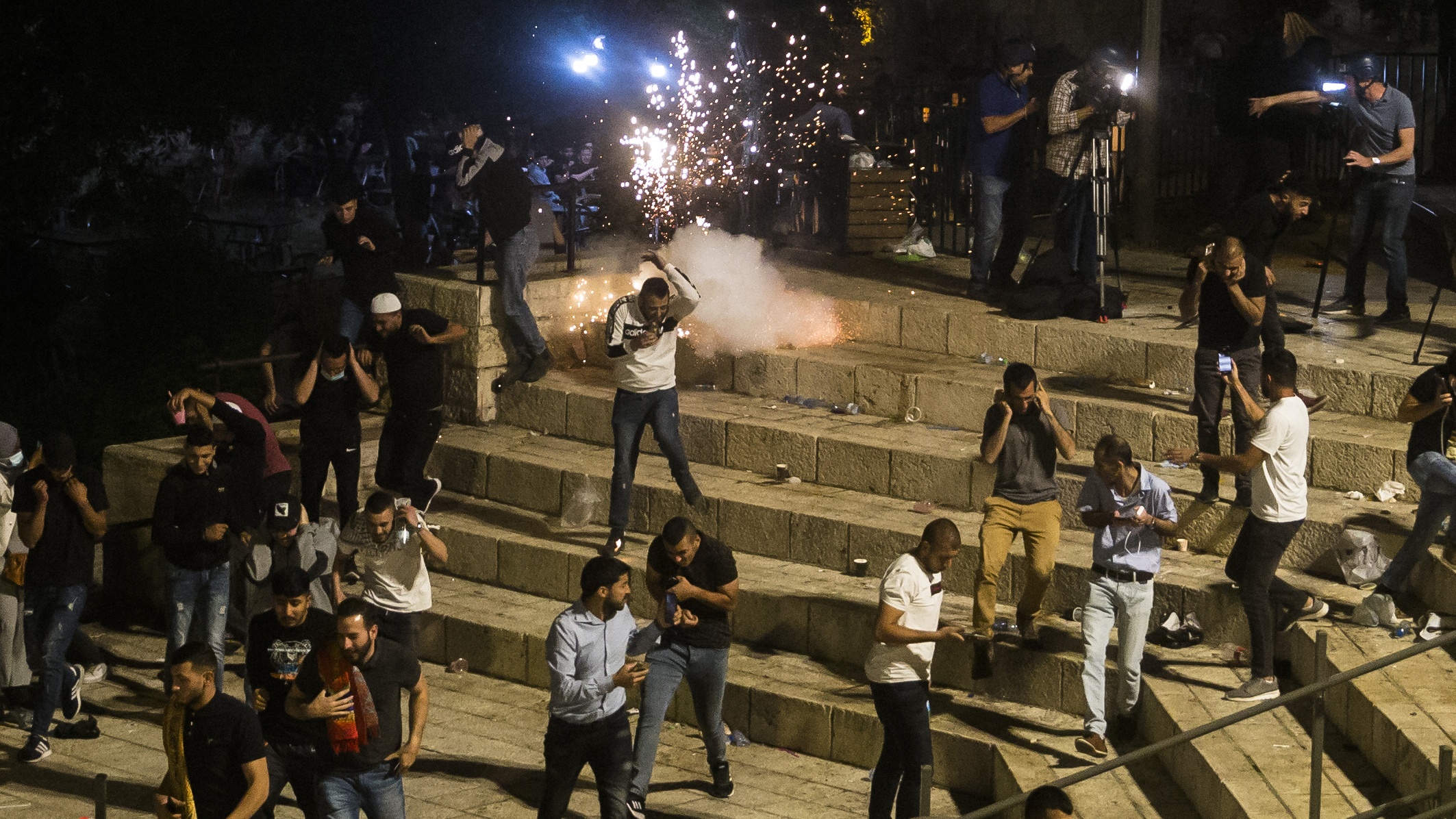 Palestinians flee a stun grenade thrown Israeli security forces near the Al-Aqsa mosque