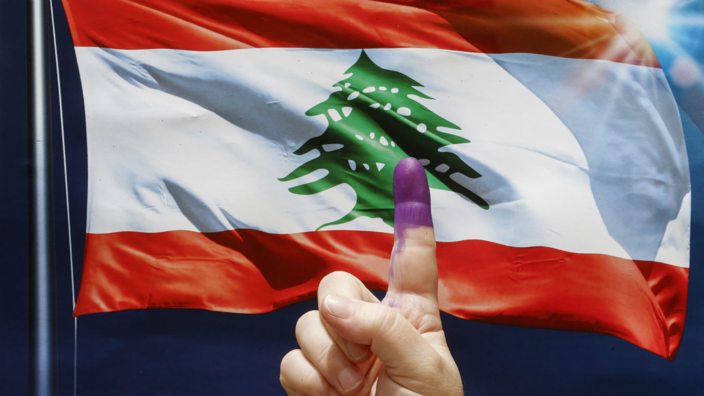 An ink-stained index finger before a poster depicting a waving Lebanese flag