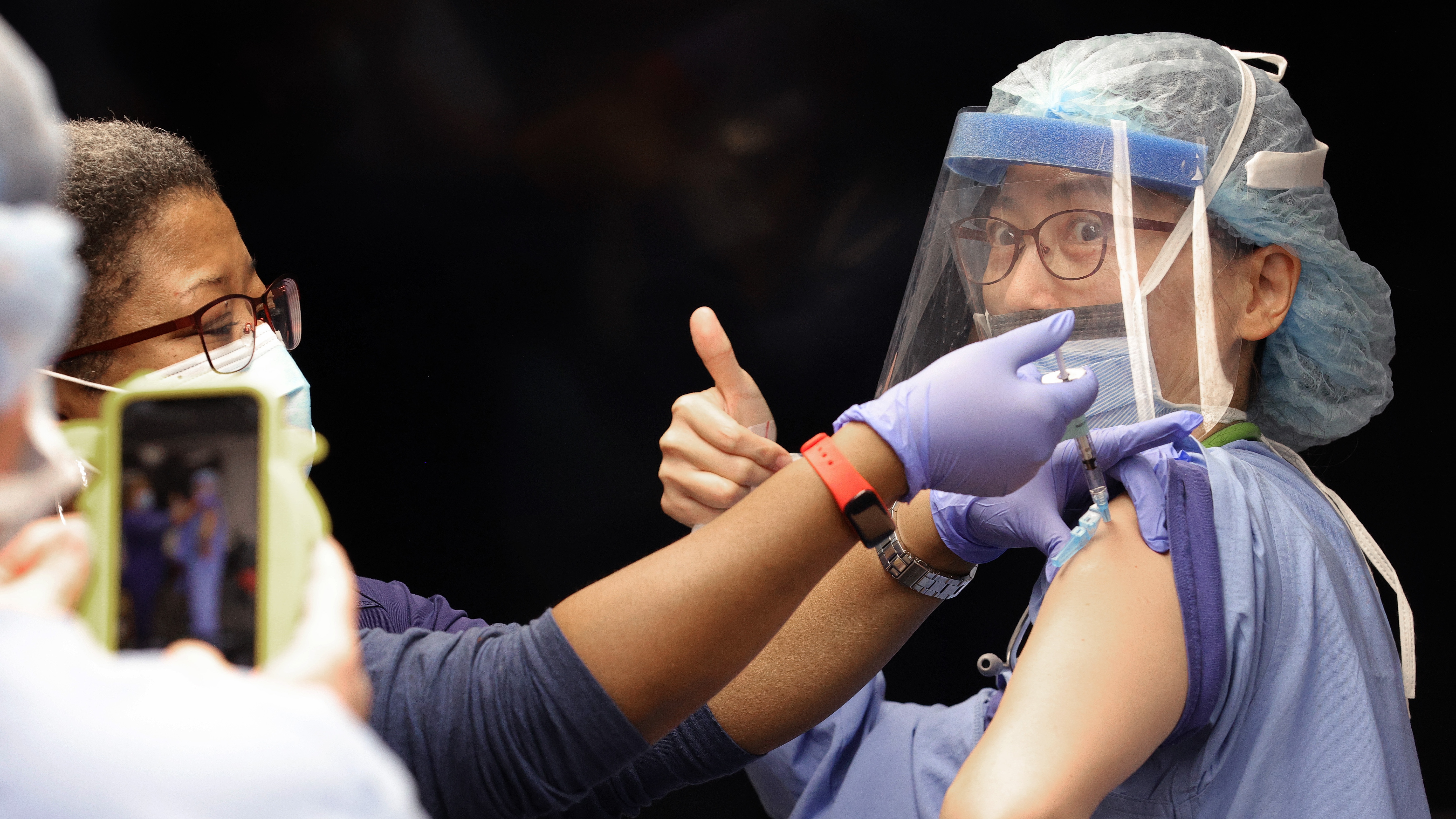 A medical worker gives a thumbs up sign as she receives the Pfizer vaccine
