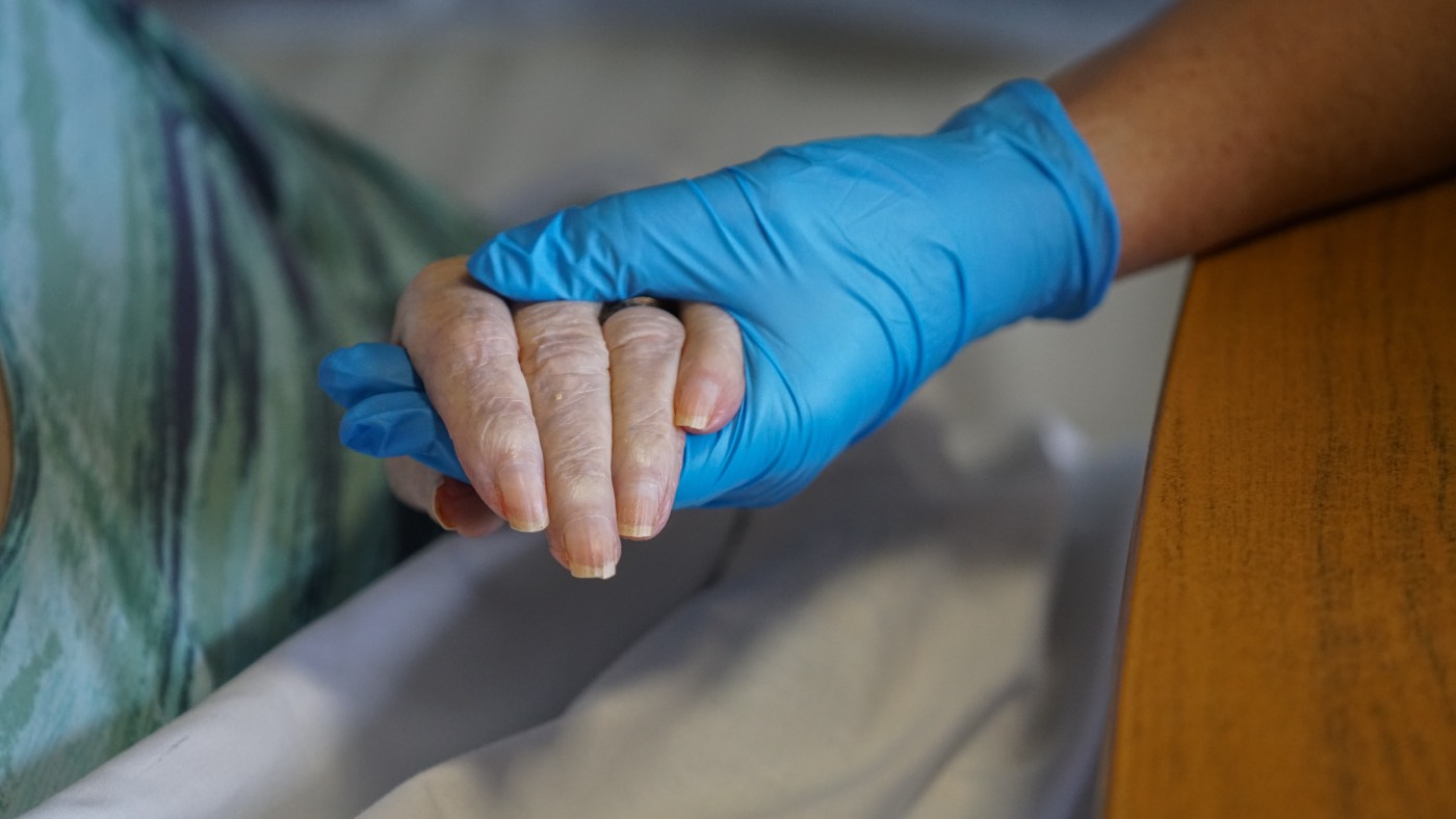  A nurse wearing PPE holds the hand of a resident in a care home