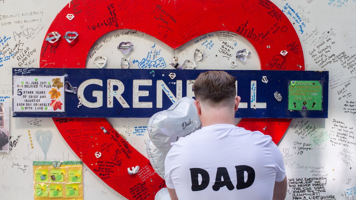 A man with ‘dad’ printed on his T-shirt leaves a tribute in front of a wall surrounding Grenfell Tower in west London