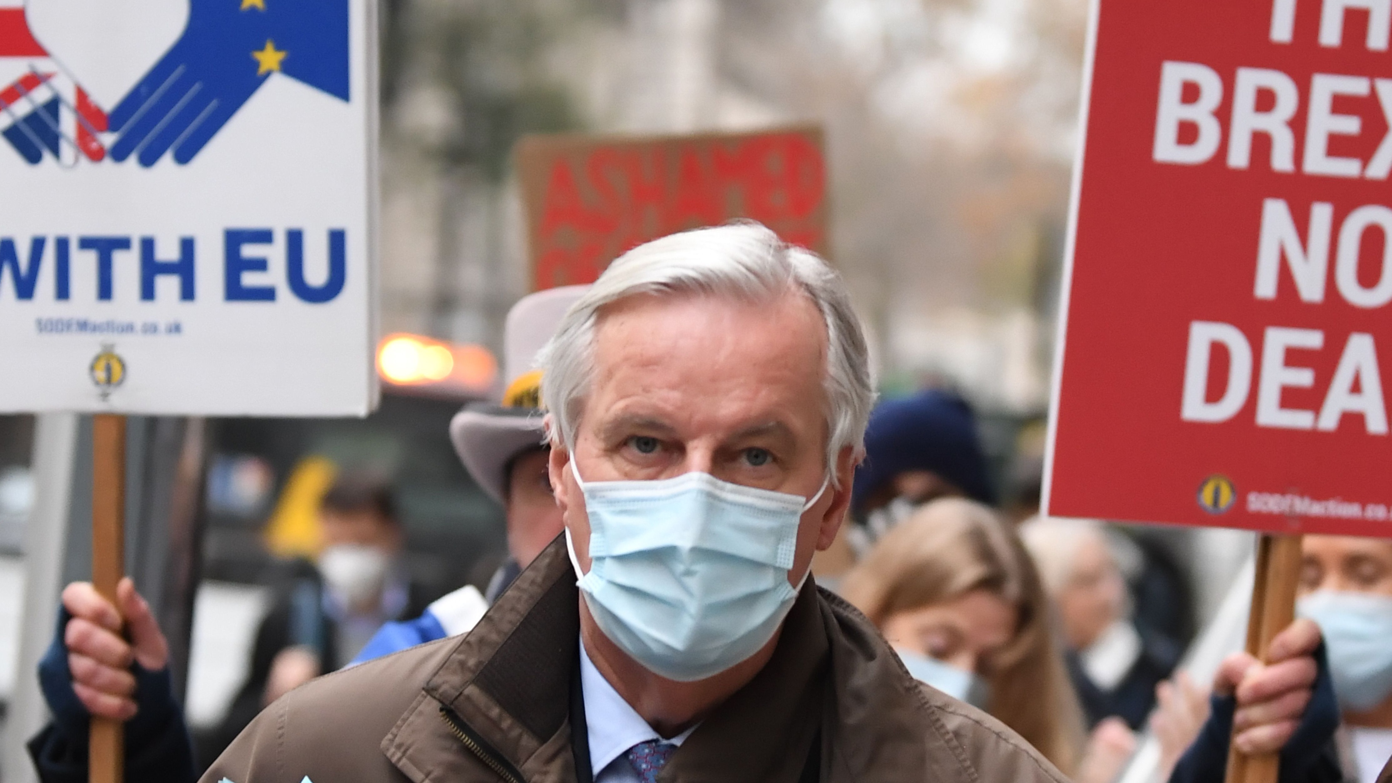 Anti-Brexit demonstrators hold placards as EU chief negotiator Michel Barnier walks through central London.