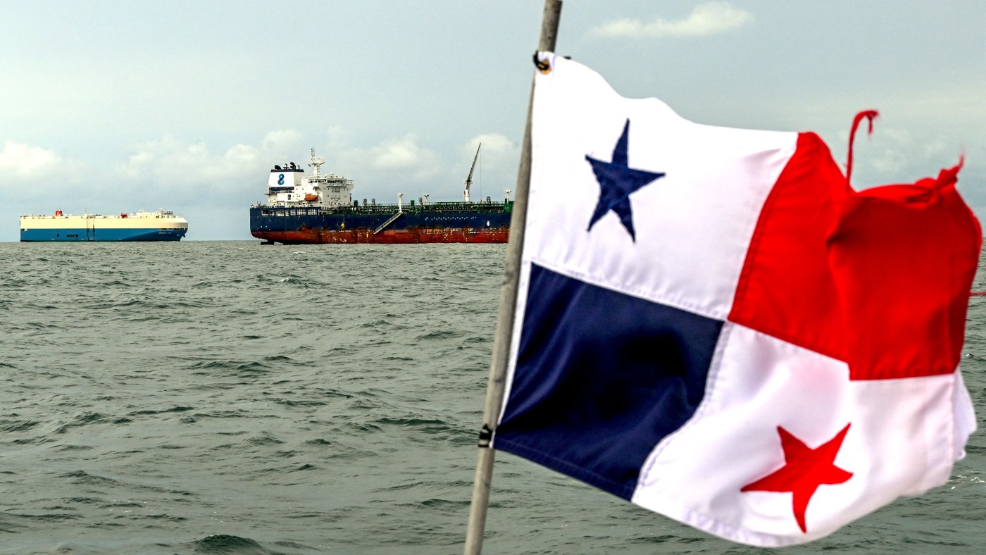 Cargo ships wait at the entrance of the Panama Canal, with a flag in the foreground