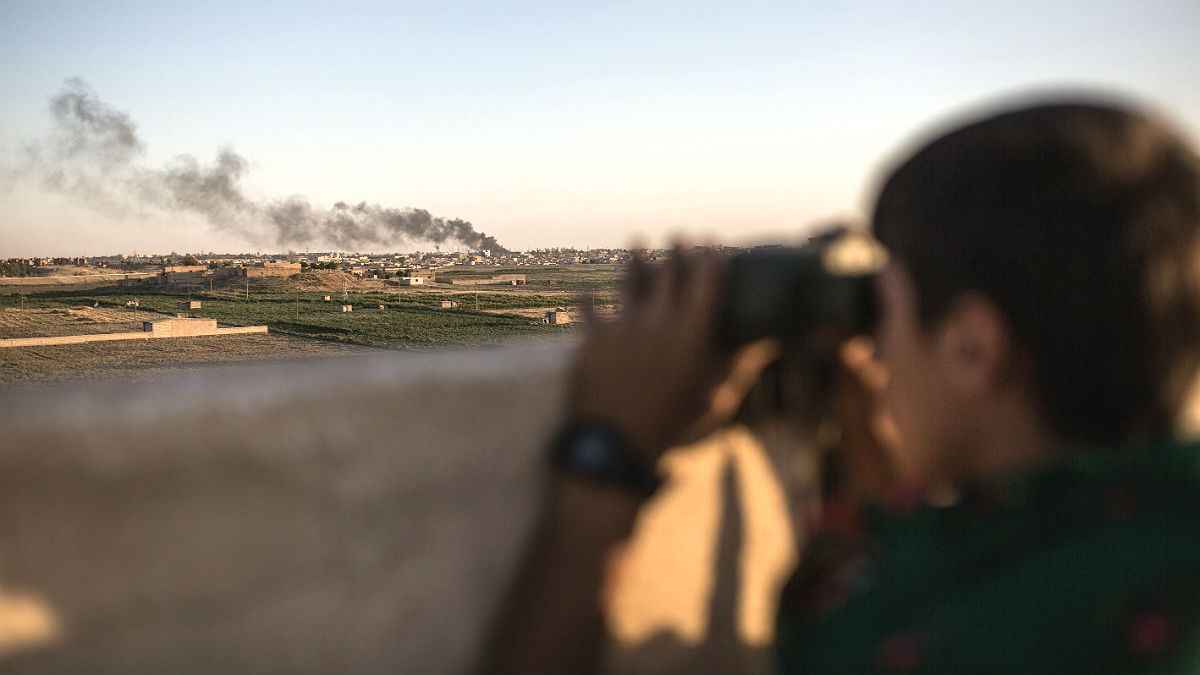 Kurdish fighters look on as their fellow soldiers clash with IS near Hasekeh, Syria