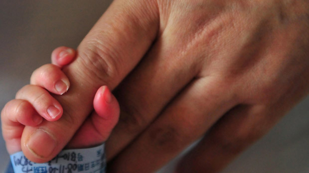 A newborn baby holds onto his mother&#039;s finger 