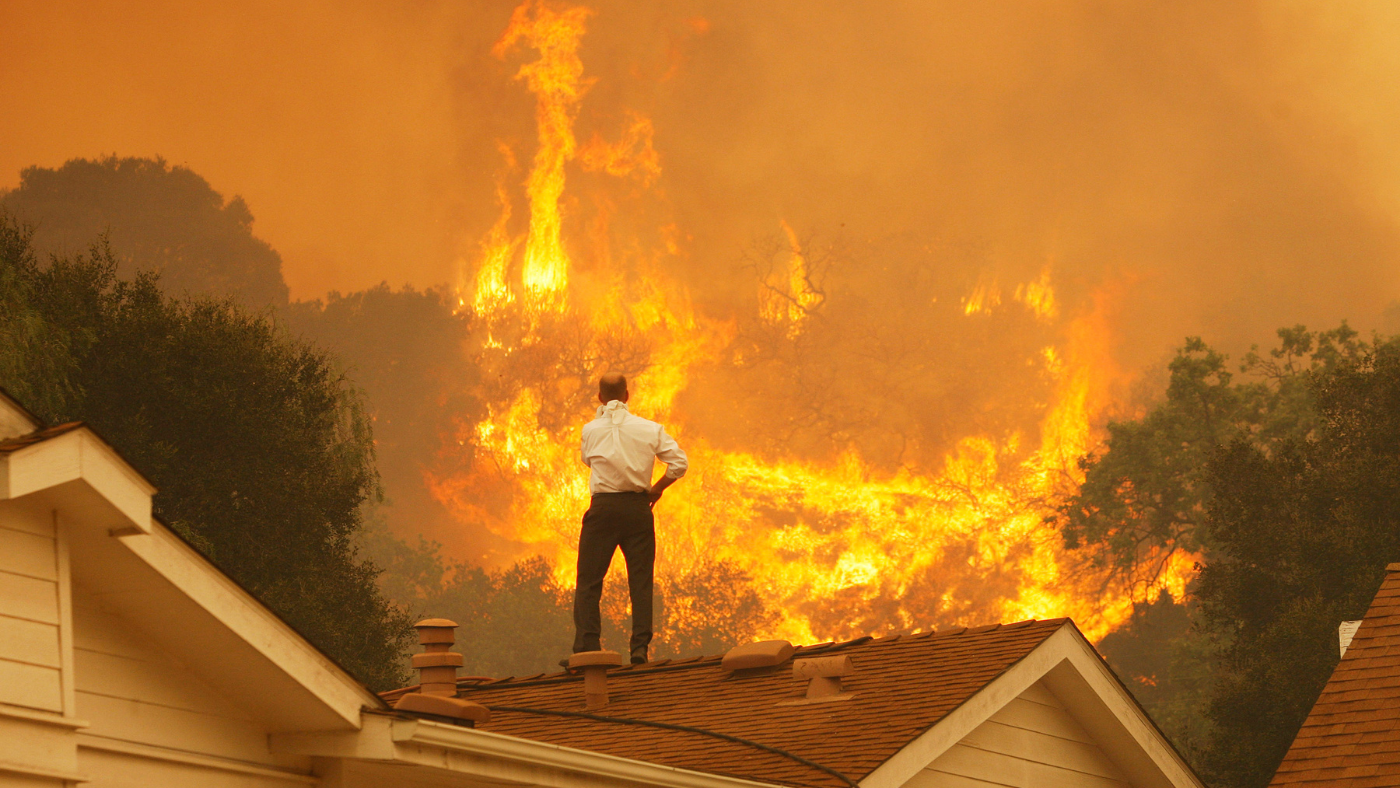 Man stands on roof watching wildfire in California