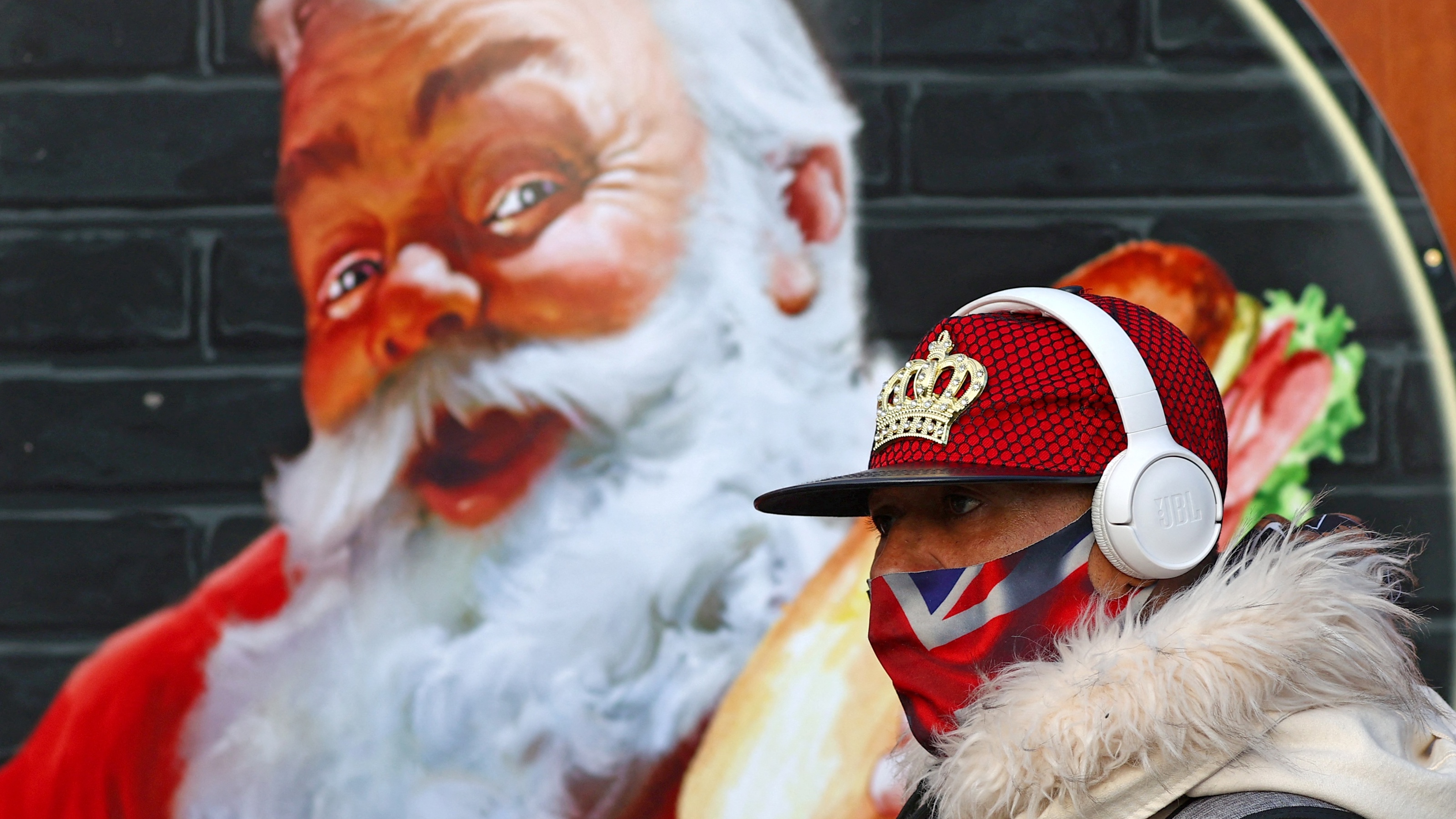 A masked man walks past an image of Santa Claus